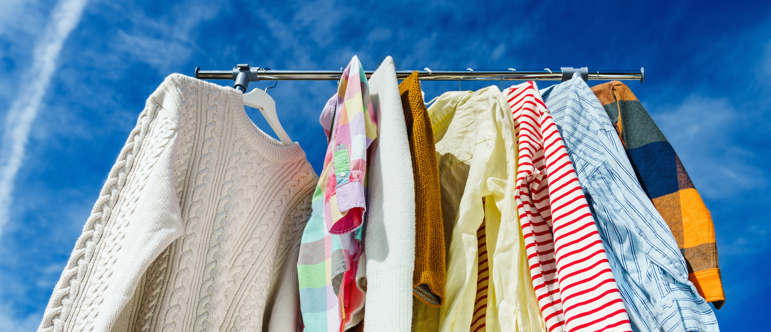 Clothing on a rack with bright blue sky in the background. Blog post explores key sustainability predictions for 2024 that could influence the future of fashion.
