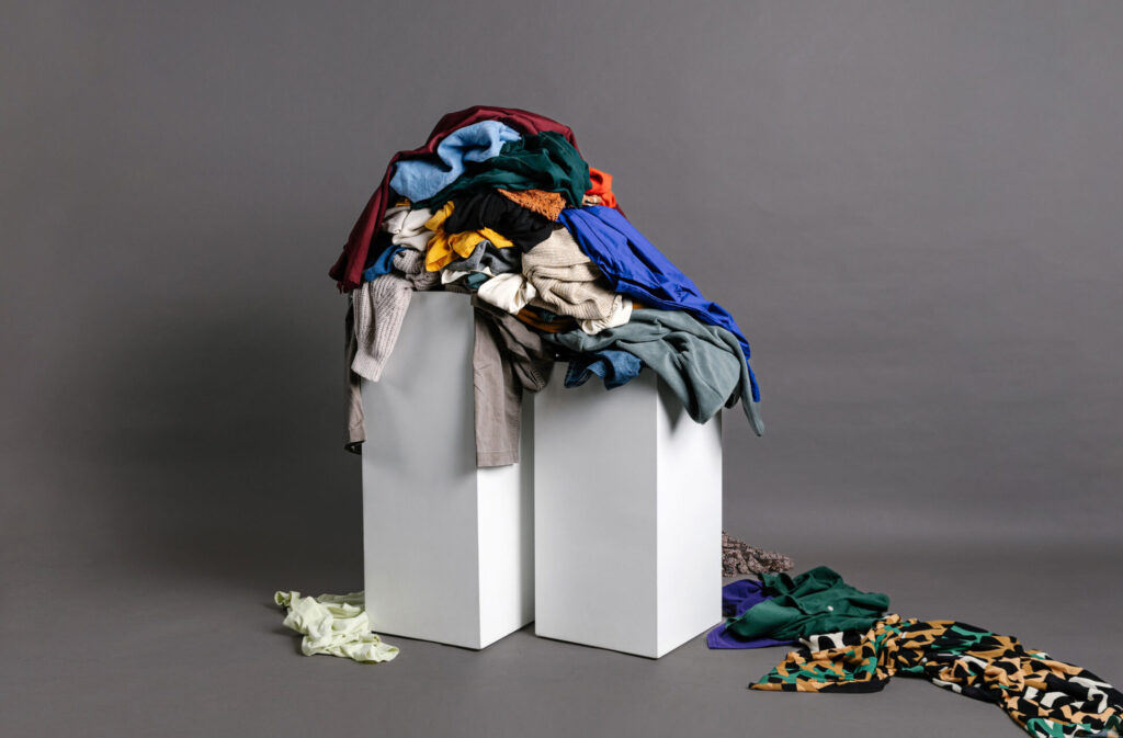 A pile of end-of-life clothes are scattered on top of two white plinths